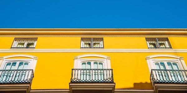 Bright facade of a typical old Mediterranean building painted in Foto de una fachada exterior de un edificio pintada de amarillo con los balcones blancos